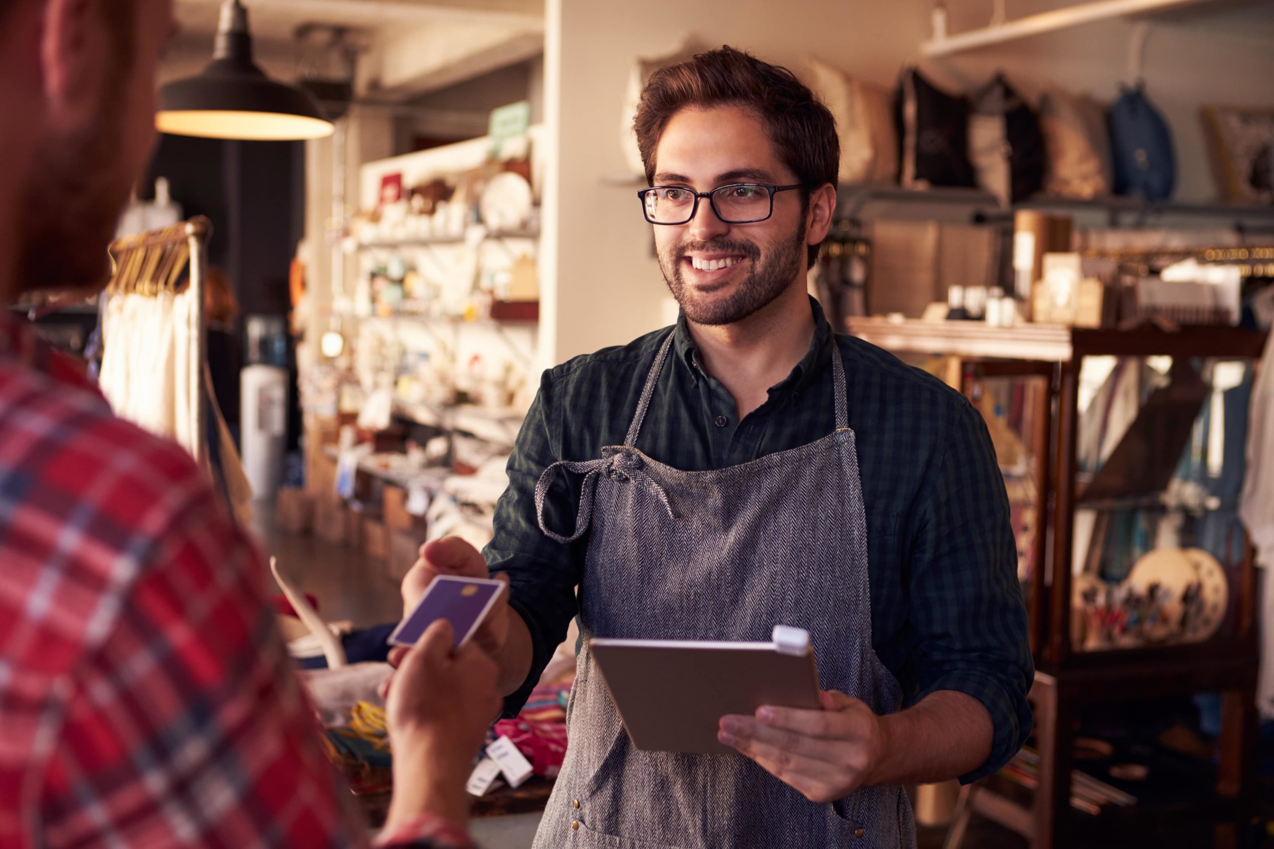 Man wearing an apron holding iPad and receiving payment from client