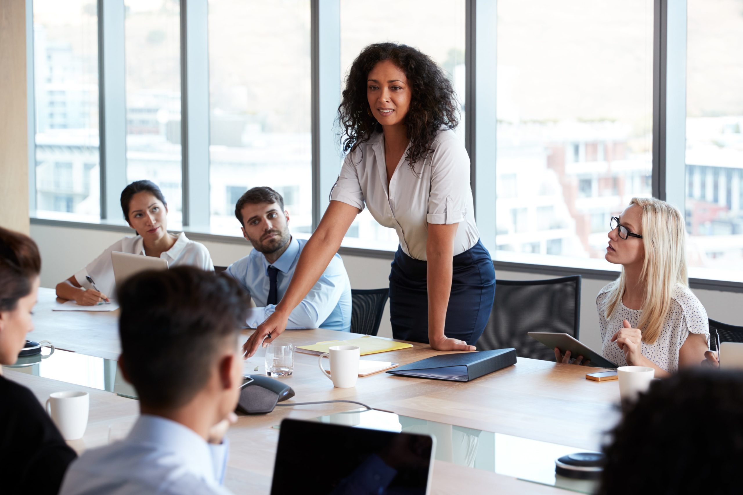 Woman standing at a table with 5 others seating and looking at her OTEC Project Management