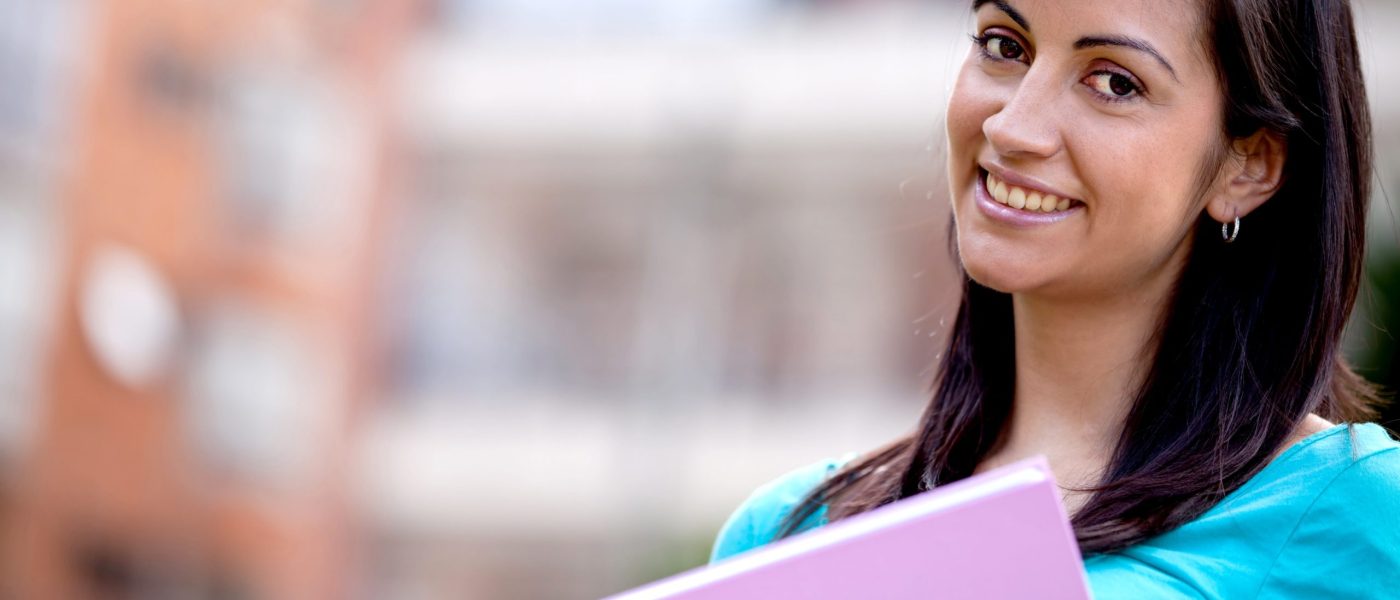 OTEC Academic Institutions - young woman smiling looking at camera holding notebook